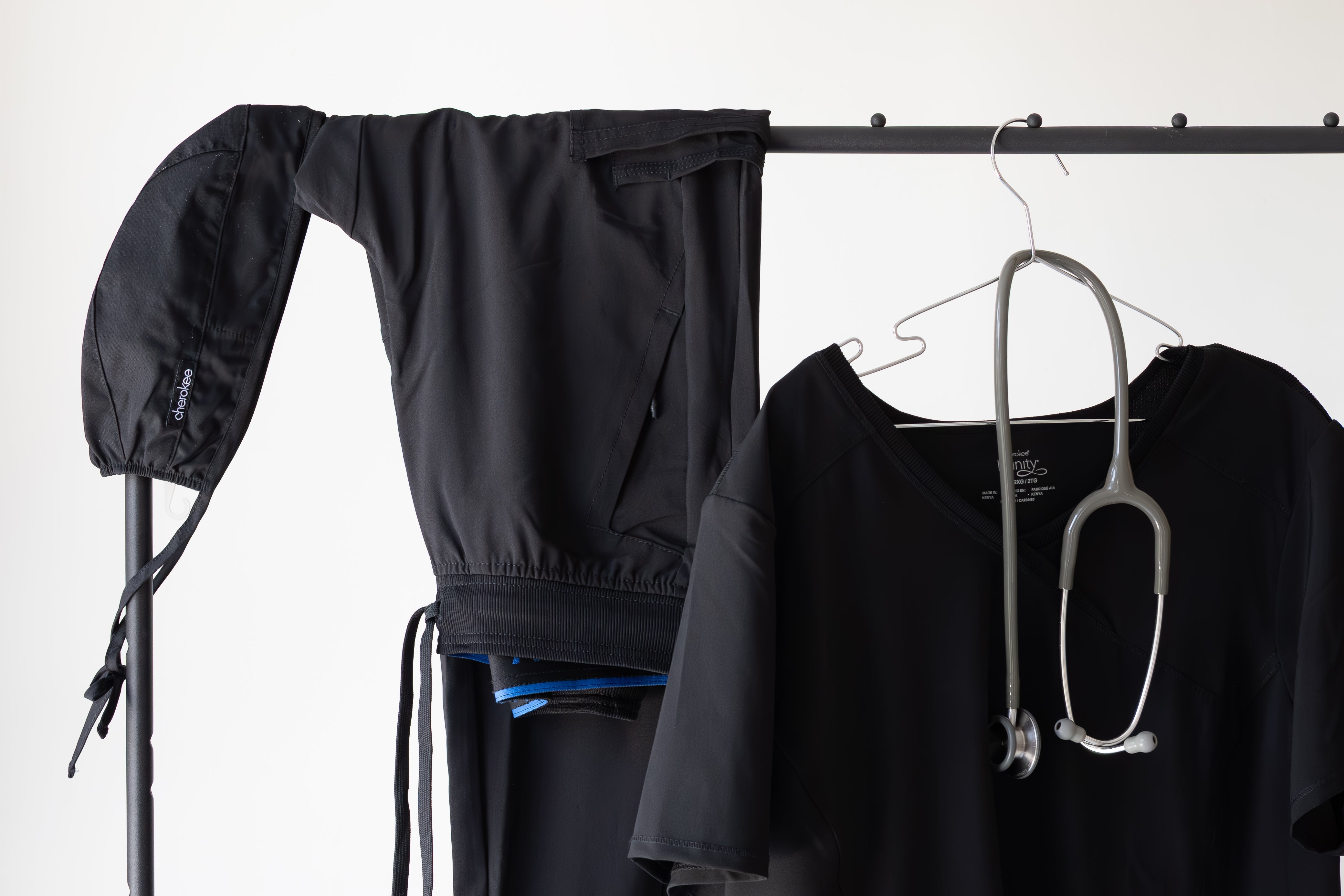 Black outfit with a stethoscope on a rack against a white background