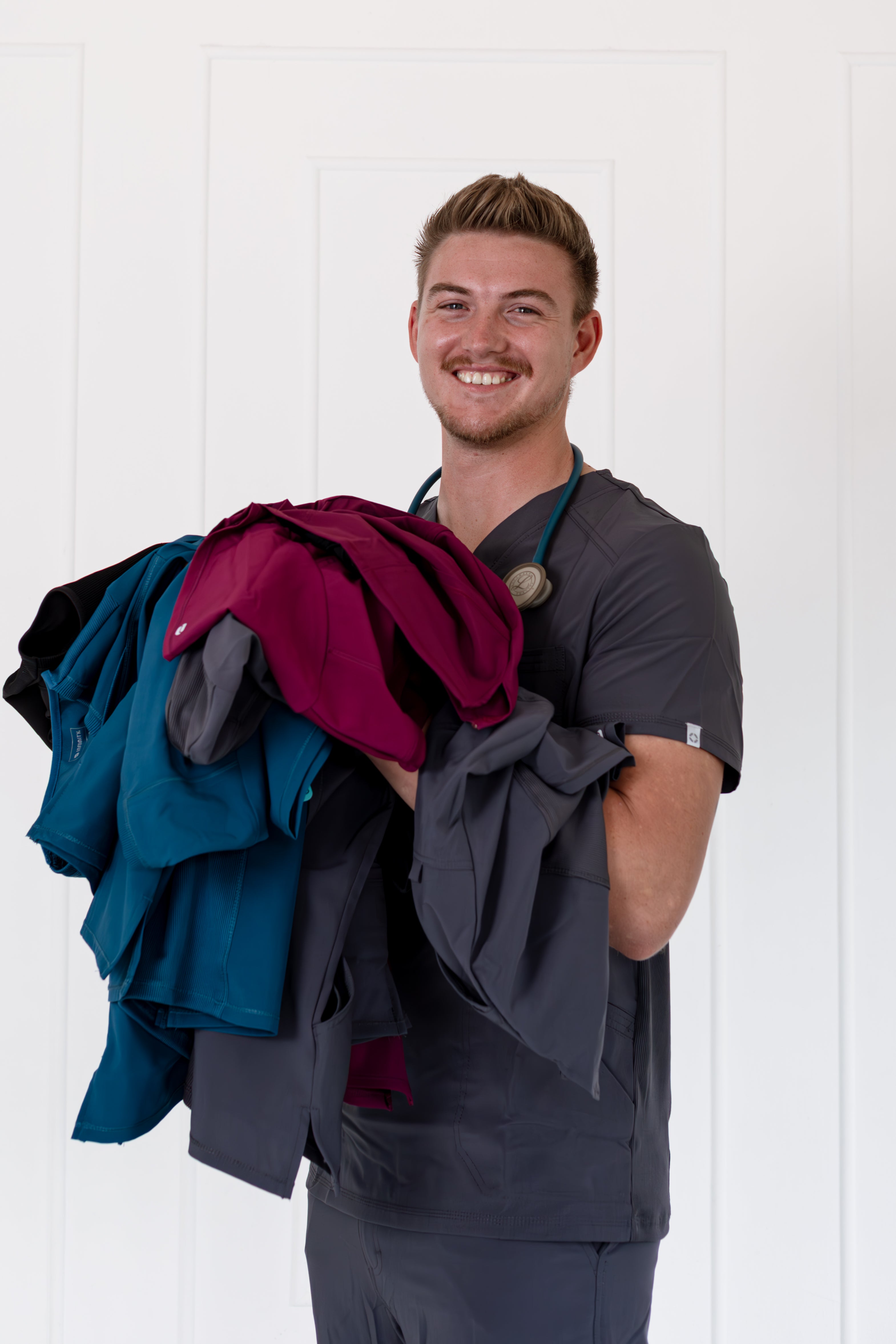 Man holding folded scrubs against a white background